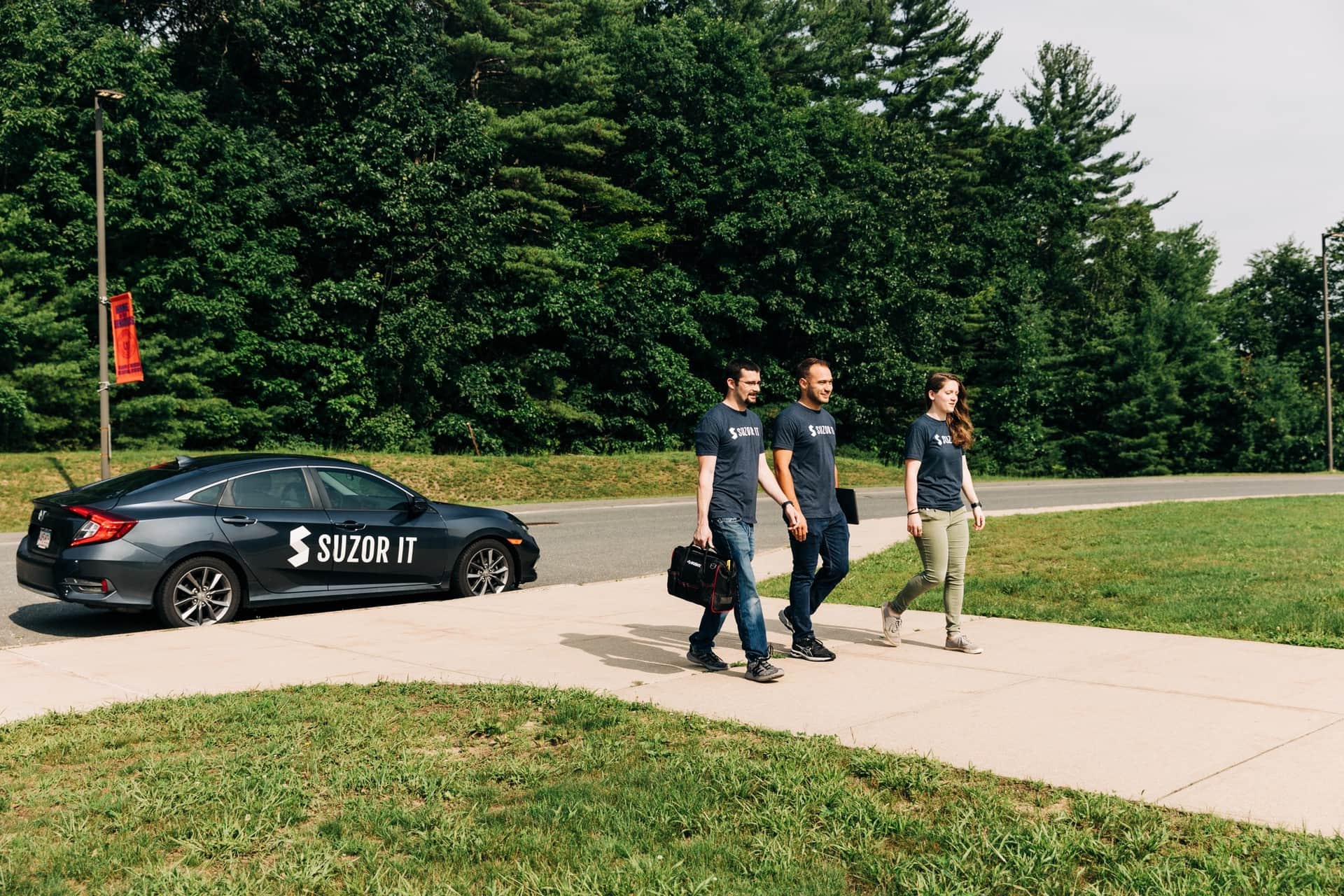 Three Suzor IT team members walking beside a branded company car